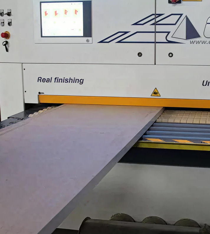 Macchinario industriale per finitura e taglio: un piano in legno scorre su guida, con indicazioni di sicurezza e area di lavorazione illuminata