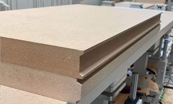 Dettaglio ravvicinato di pannelli in materiale composito e legno, con bordo rifinito e struttura industriale sullo sfondo, su banco di lavoro